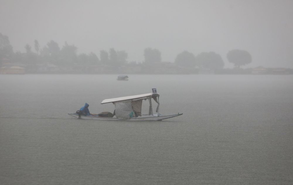A boatman pulls his boat on Dal waters as rains lash Srinagar on Thursday