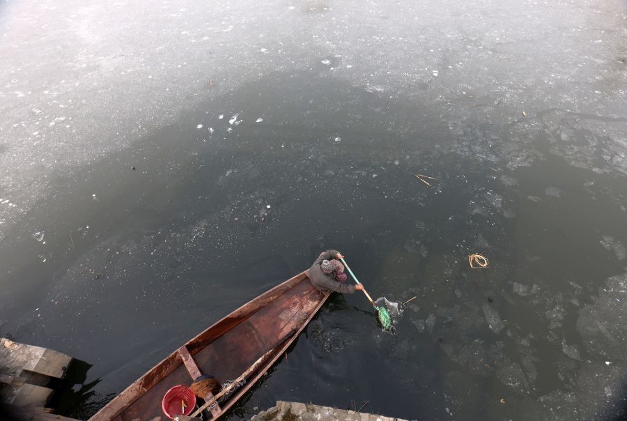 A boatman navigates through frozen waters of Dal Lake on Thursday in Kashmir reels under severe cold and dry conditions